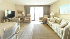 Een hotelkamer met een televisie, twee fauteuils, een bank, een eettafel en een groot raam.