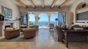 Amplia sala de estar con muebles de mimbre, chimenea y vista al océano.