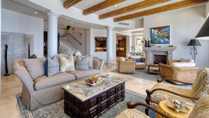 Amplia sala de estar con techo alto, vigas de madera, chimenea y escalera que lleva a otras habitaciones.