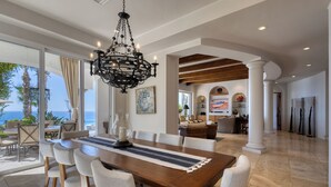 Un comedor amplio con una larga mesa de madera, sillas blancas con tapicería y un candelabro negro.