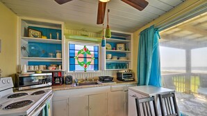 A compact kitchen with white cabinets, a stove, microwave, and a coffee maker. There is a window with a decorative glass and a view of the outdoors. - Steps to Gulf! Pet-Friendly Galveston Getaway (Galveston)