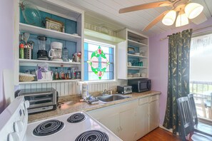A kitchen with a stove, toaster, sink, and various kitchen items on shelves. - Steps to Private Beach! Pet-Friendly Getaway (Galveston)