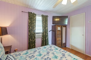Un dormitorio con cama, cómoda, televisor y ventana con cortinas.