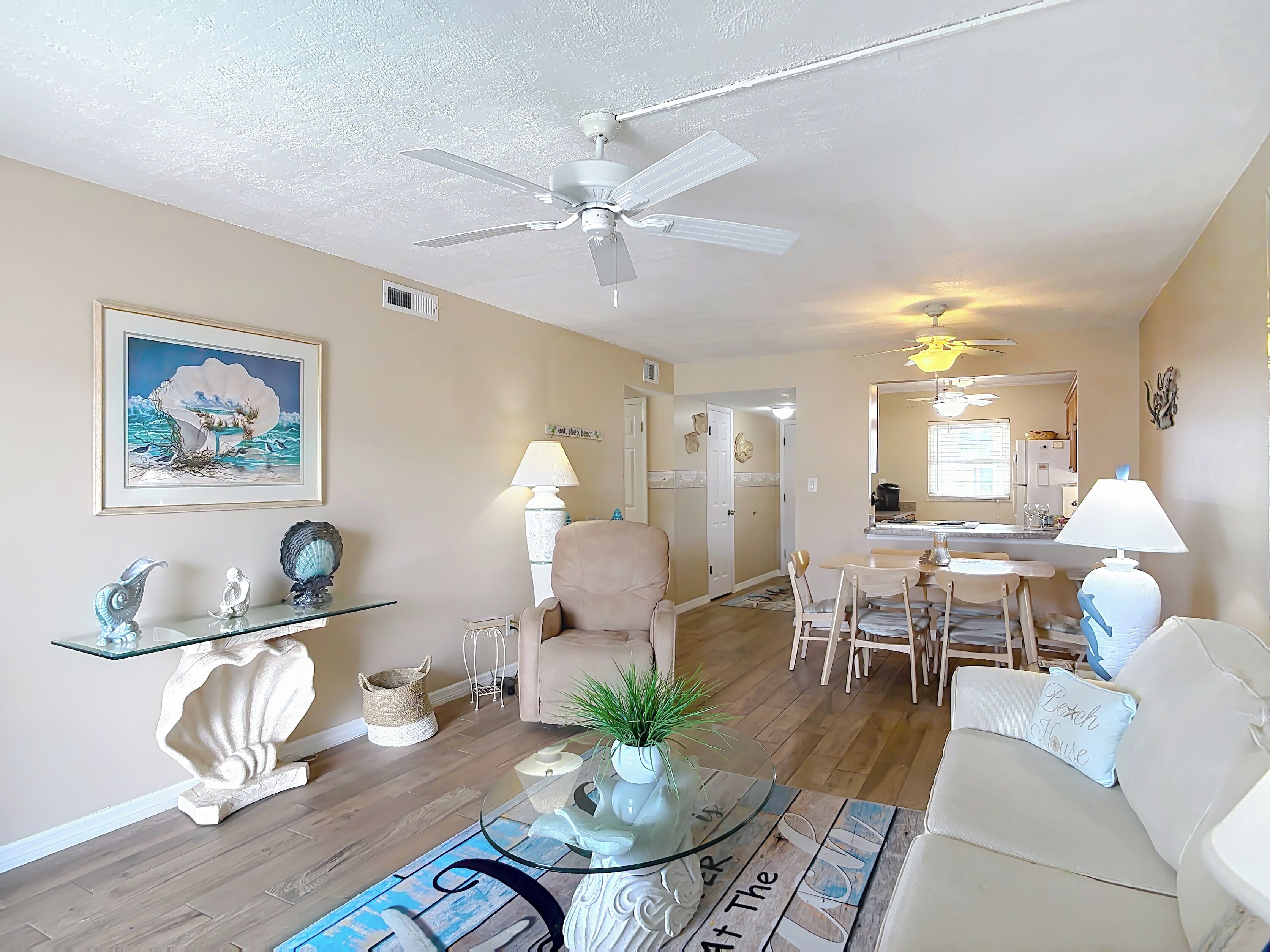 A living room with a glass coffee table, beige sofa, and a dining area with a table and chairs.