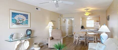 A living room with a glass coffee table, beige sofa, and a dining area with a table and chairs.