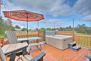 Een houten terras met een jacuzzi, tuinmeubels en een lichtslingering.