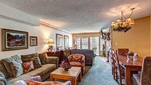 A cozy living room with a sofa, chairs, a coffee table, and a dining table. There is a fireplace with a TV on the wall, and a chandelier hanging above the table. - Fantastic Breckenridge Amenities! Perfect Condo for Hiking/Biking/Ski Access! Mo (Breckenridge)