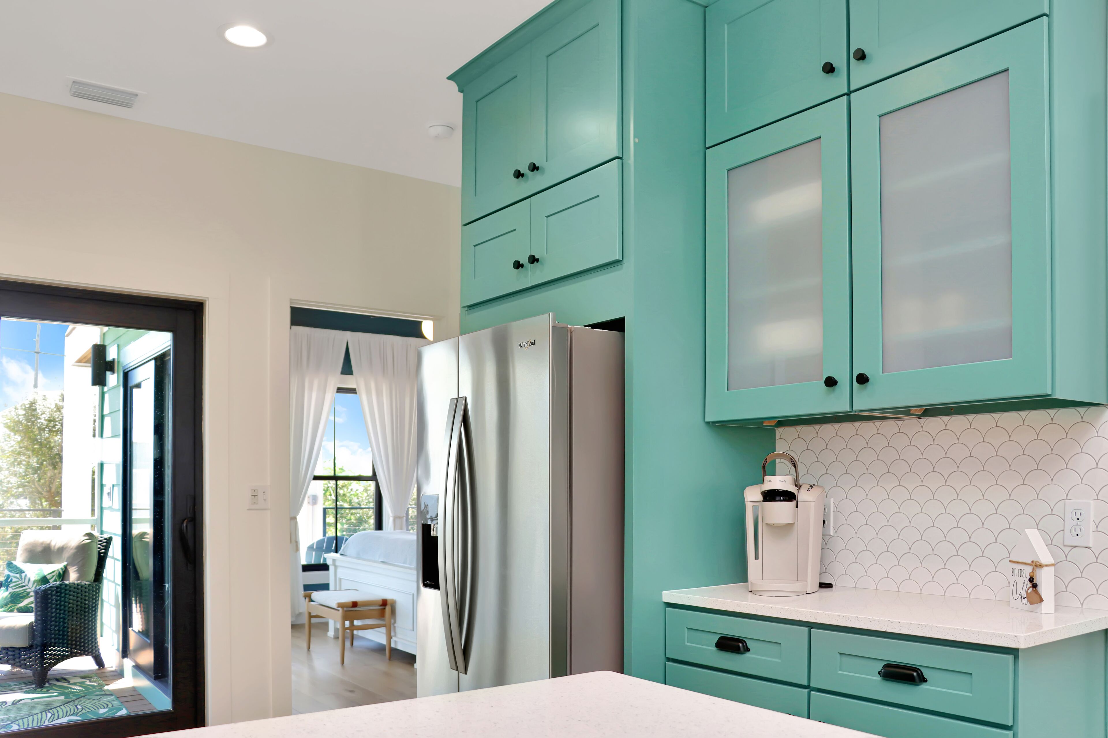 A modern kitchen with teal cabinets, a stainless steel refrigerator, and a white countertop.
