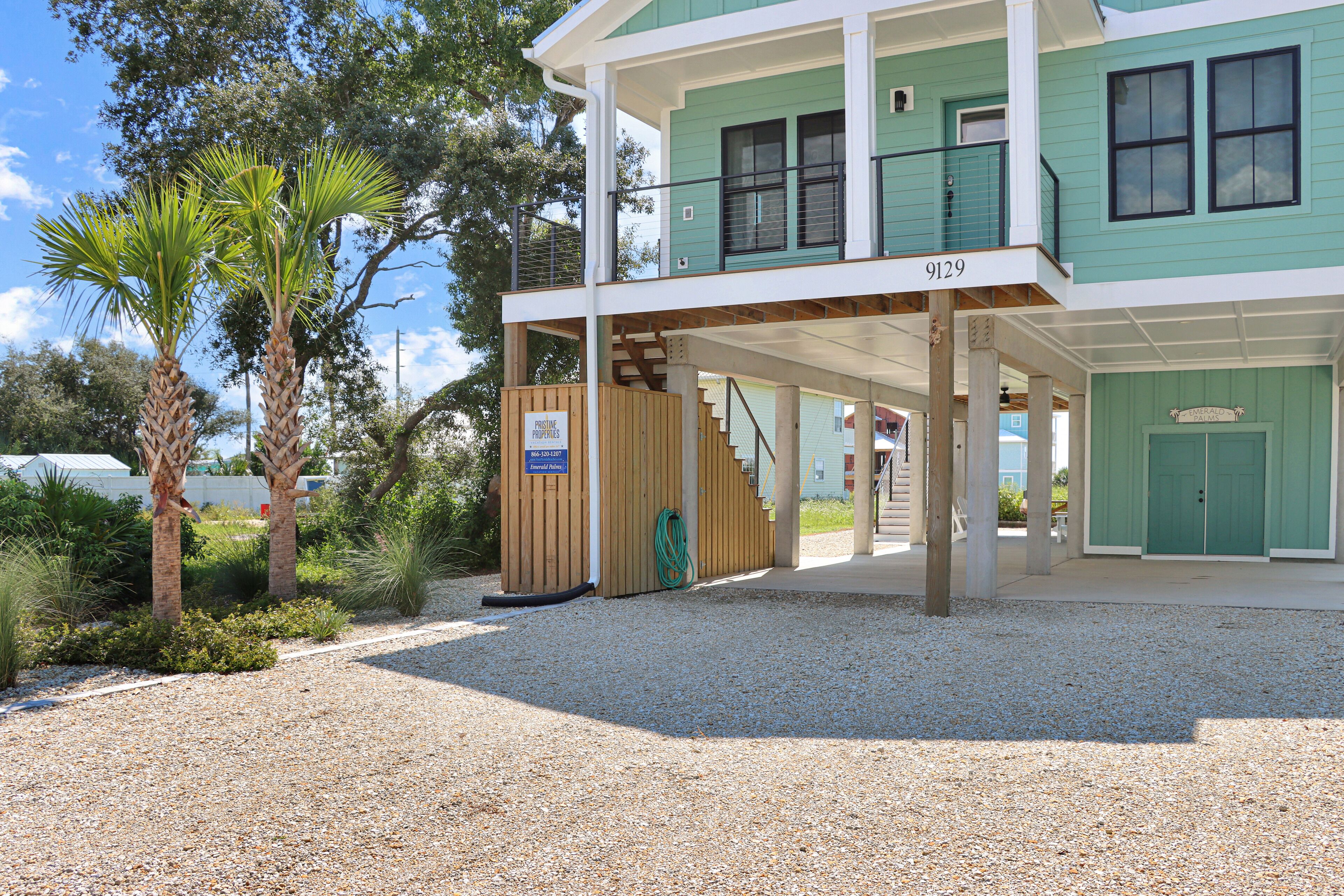 A two-story building with a green exterior, a wooden staircase leading to the upper level, and a gravel driveway.