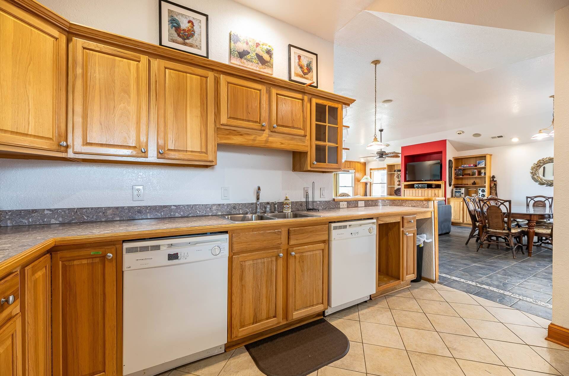 A kitchen with wooden cabinets, a dishwasher, and a dining area with a TV and chairs.