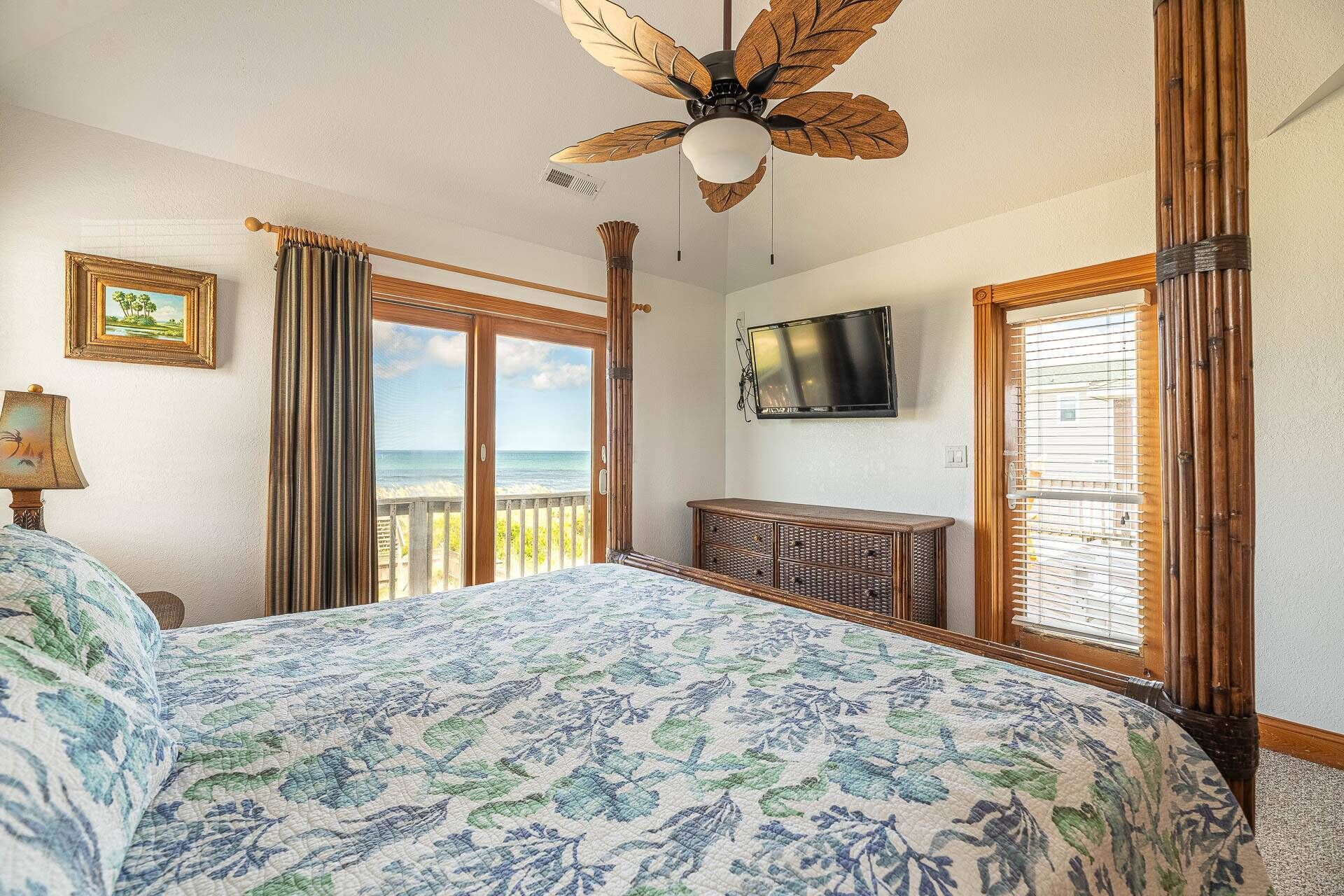 Een slaapkamer met een groot bed, een plafondventilator, een televisie en uitzicht op de oceaan.