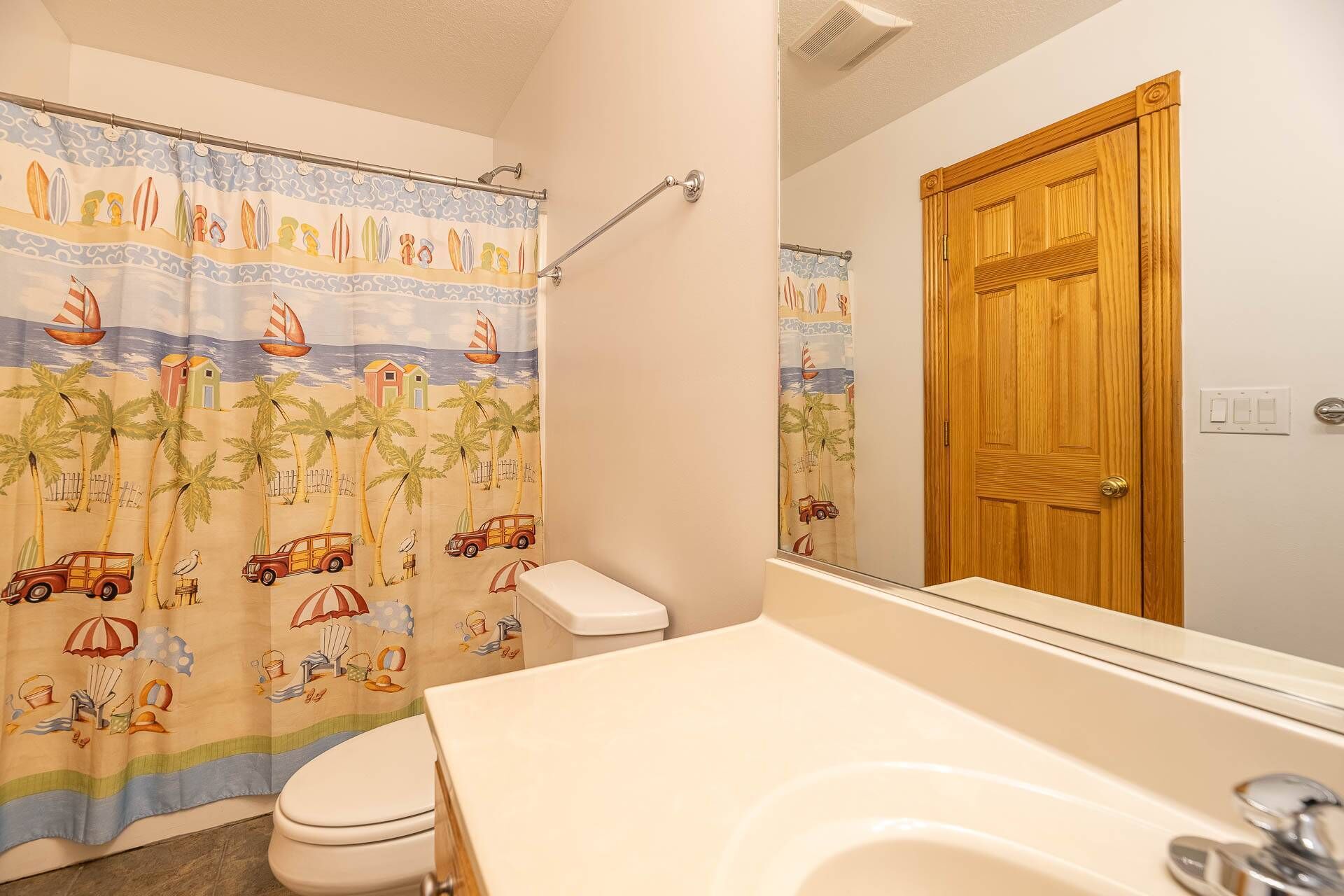 A bathroom with a beach-themed shower curtain, a wooden door, and a white sink.