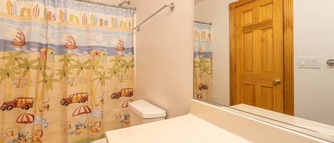 A bathroom with a beach-themed shower curtain, a wooden door, and a white sink.