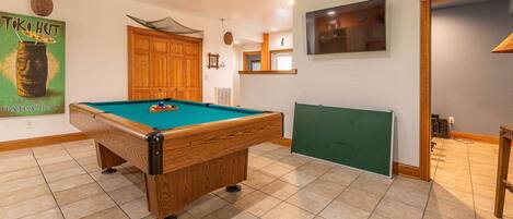 Una mesa de billar en una habitación con armarios de madera, una pizarra verde y un cartel en la pared.