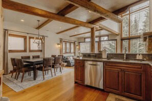 A spacious kitchen with wooden beams, a dining area with a table and chairs, and a view of trees outside.