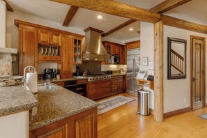 A kitchen with wooden cabinets, granite countertops, stainless steel appliances, and a wooden ceiling beam.