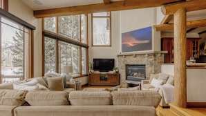 Una sala de estar acogedora con chimenea de piedra, un televisor y un ventanal con vistas a árboles.