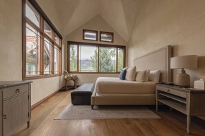 A bedroom with a large window, a bed, a nightstand, and a dresser.