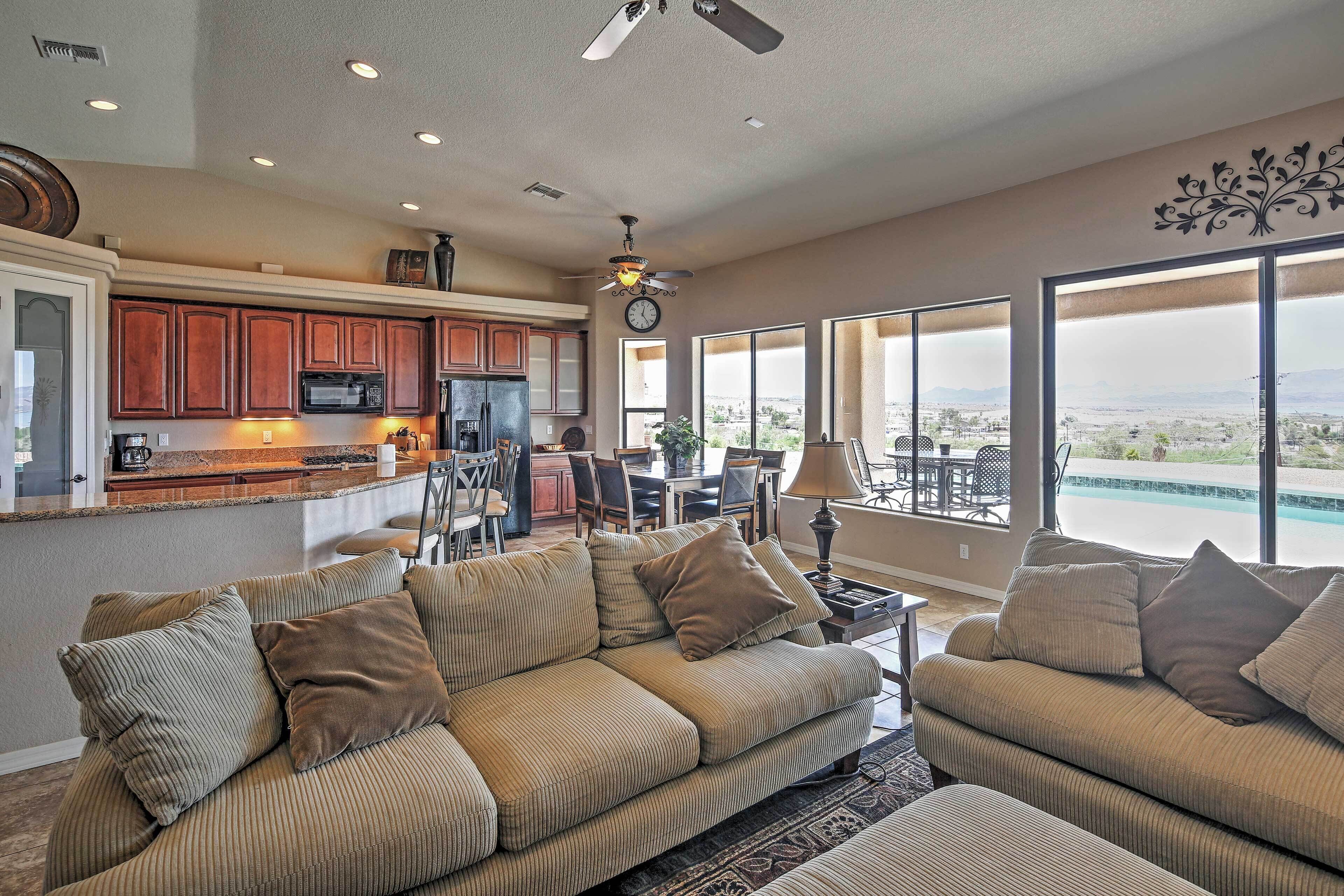 A spacious living room with a large sectional sofa, a kitchen with wooden cabinets, and a dining area with a view of the mountains.