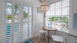 A bright room with white shutters, a chandelier, and a table with chairs.
