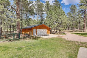 A single-story wooden cabin with a garage, surrounded by a forested area. - Private Black Hills Home w/ Corral: Horses Welcome (Custer)