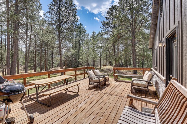 A wooden deck with picnic tables and chairs, surrounded by tall pine trees. - Private Black Hills Home w/ Corral: Horses Welcome (Custer)