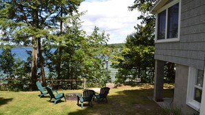 Ein Garten mit Blick auf einen See, drei Adirondack-Stühle und eine Feuerstelle.