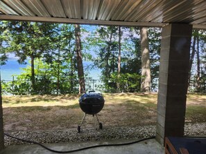 Un espacio exterior techado con una parrilla, vista a un lago y zona boscosa.