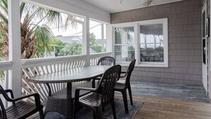 Une terrasse couverte avec une table ronde et des chaises, des rampes blanches et une vue sur l’extérieur.