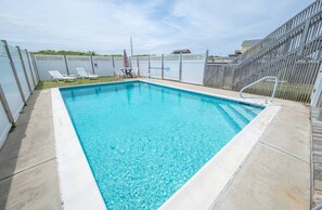 Une piscine rectangulaire à l’eau d’un bleu limpide, entourée d’une clôture blanche et d’une terrasse en bois.