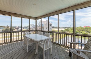 A covered outdoor deck with a table and chairs, large windows, and a view of surrounding houses. - Fun 'N Sun - Nags Head MP 16, 250 Ft to Beach Access, Pool, Pets OK, YR Flex Stays (Nags Head)