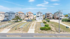 A coastal residential area with multiple two-story houses, a parking lot, and a clear view of the ocean. - Fun 'N Sun - Nags Head MP 16, 250 Ft to Beach Access, Pool, Pets OK, YR Flex Stays (Nags Head)