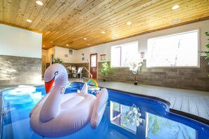 Ein Hallenbad mit einer Schwaneinattreibe, einem Regenbogen-Schwimmreifen und Blick ins Freie durch große Fenster.