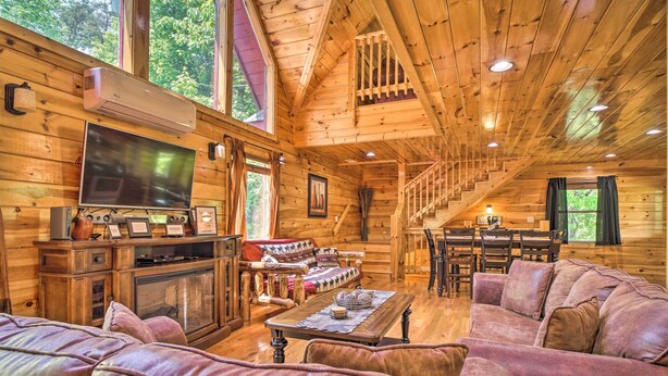 A log cabin interior with a living room, dining area, and a staircase. - Saltwater Pool & Mtn-View Deck: Pigeon Forge Cabin (Sevierville)