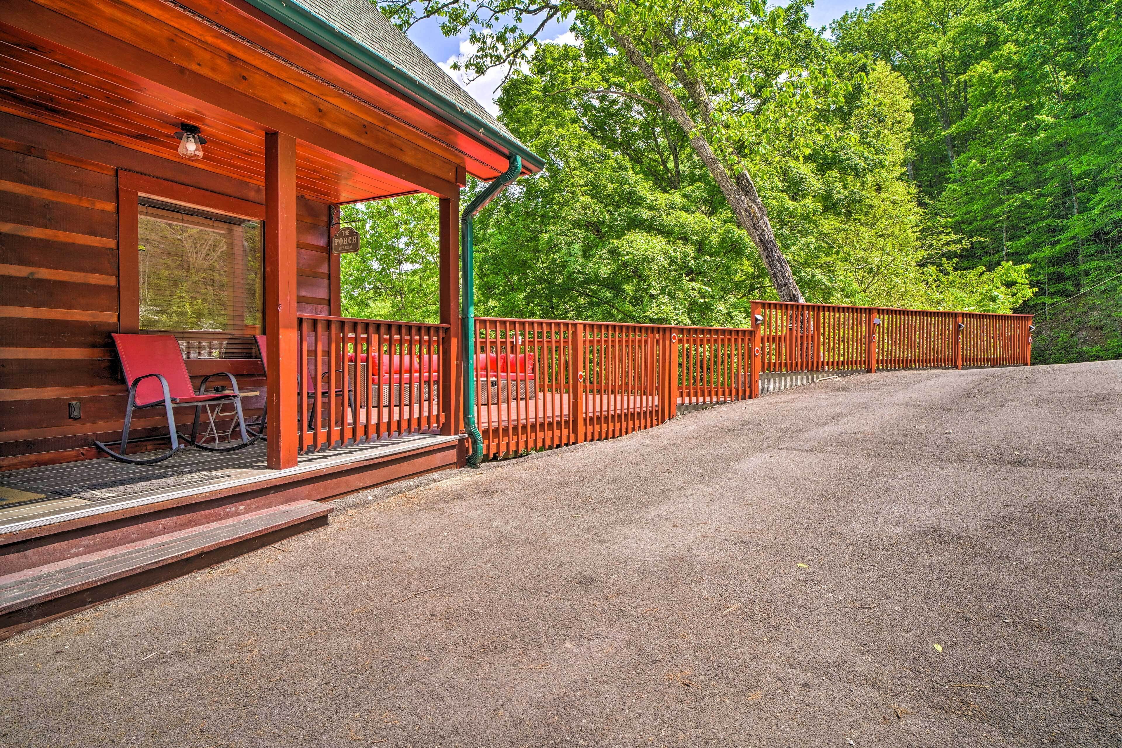 A wooden cabin with a porch, a red chair, and a gravel driveway.
