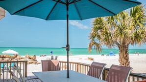 Eine Terrasse am Strand mit Tisch und Stühlen mit Blick auf einen Sandstrand und türkisfarbenes Wasser.
