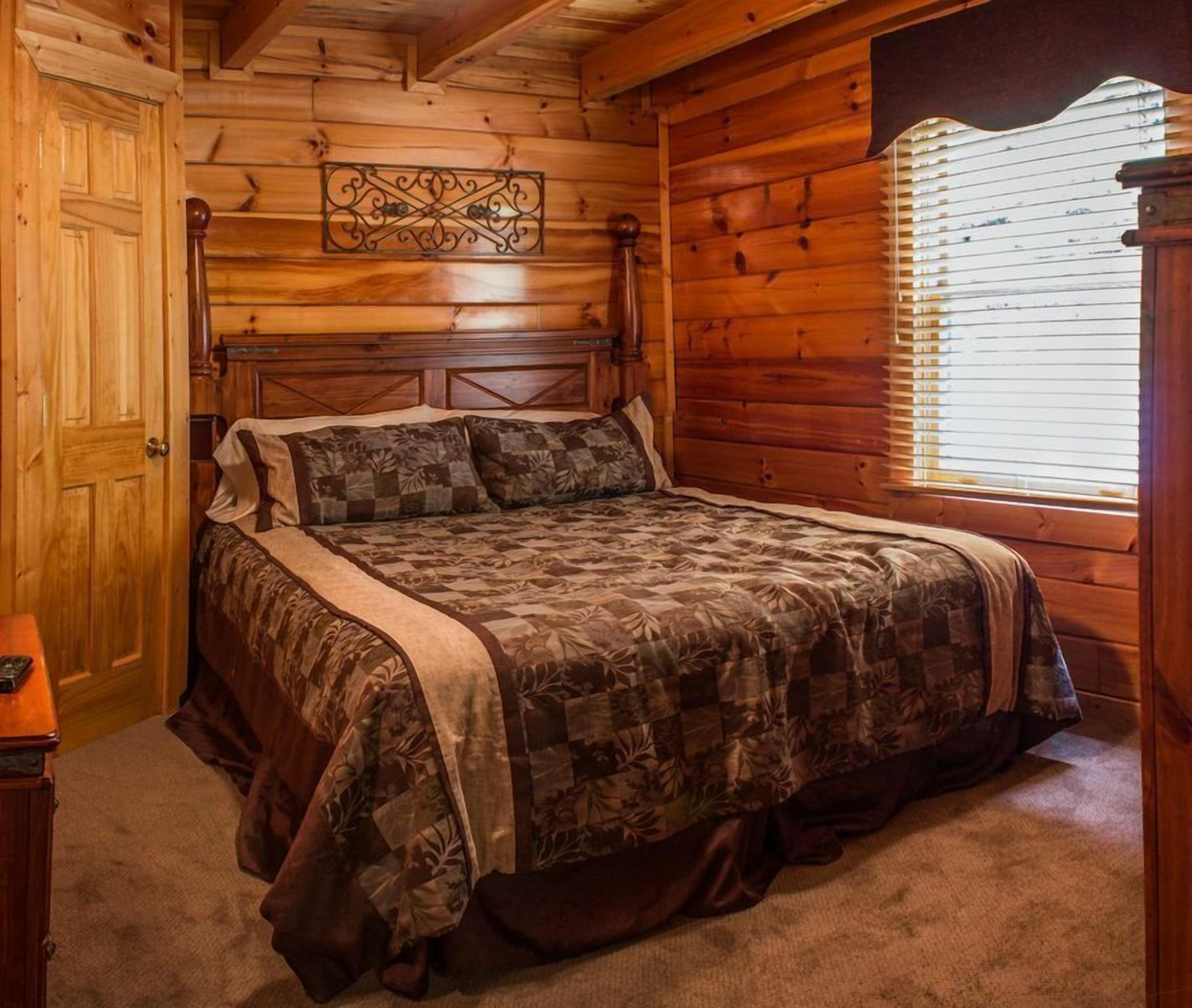 Een slaapkamer met houten lambrisering, een bed, een nachtkastje en een raam met jaloezieën.