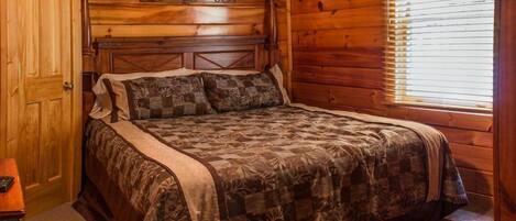 Een slaapkamer met houten lambrisering, een bed, een nachtkastje en een raam met jaloezieën.