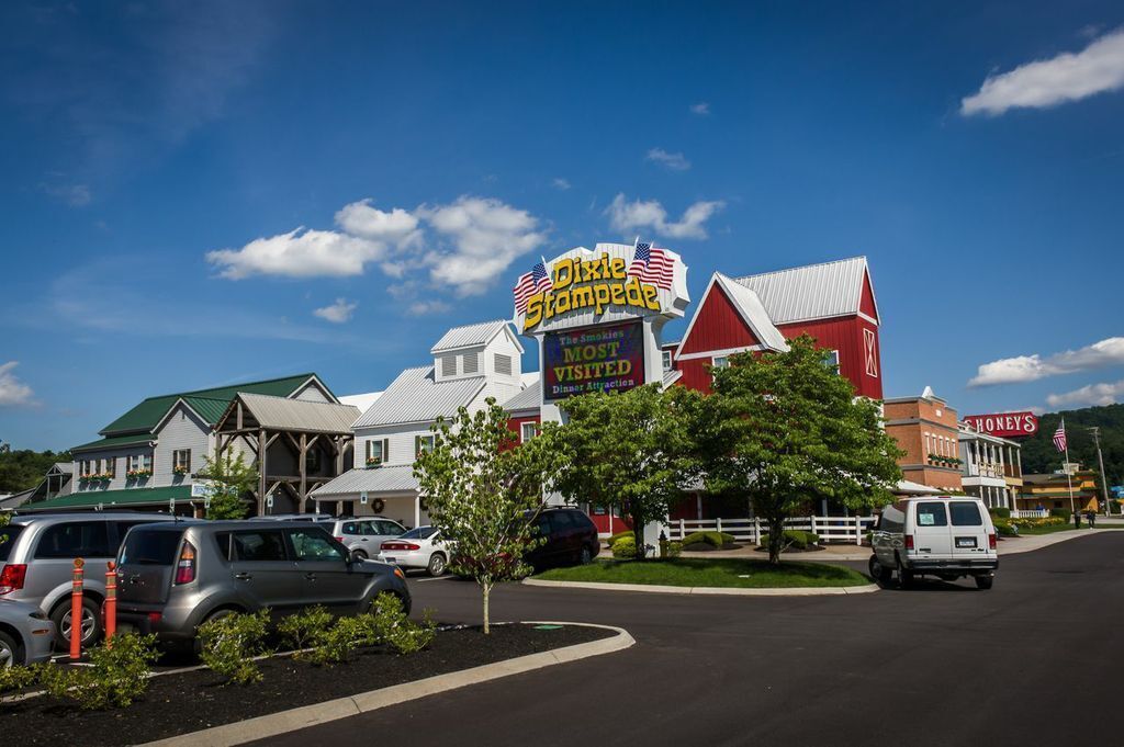 Un restaurante llamado Dixie Stampede con un llamativo letrero de la bandera estadounidense, rodeado de otros edificios y coches estacionados.