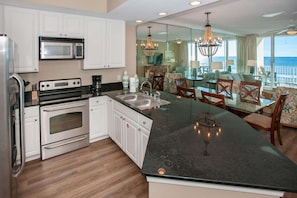 Enjoy meals in the spacious kitchen with a large island, double oven, and microwave, adjacent to a dining area with a glass-top table.