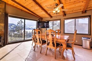 Un comedor con mesa y sillas de madera, ventanas amplias con vista a la montaña y un ventilador de techo.