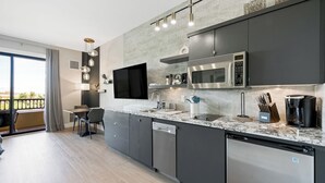 A modern kitchen with a built-in microwave, oven, and dishwasher, a dining area with a table and chairs, and a large window offering a view of the outdoors.