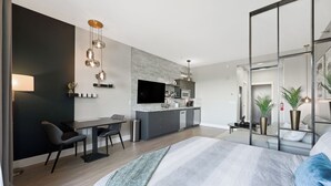 A modern, well-lit bedroom with a large bed, a desk, and a kitchenette area.