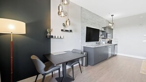 A modern kitchen with a dining area, featuring a dark wall, light wood flooring, and contemporary pendant lighting.