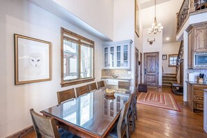 Un comedor con mesa de vidrio, sillas de madera y una araña.