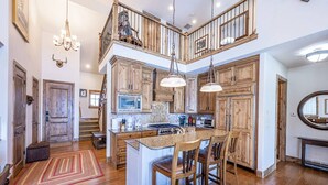 A spacious kitchen with wooden cabinetry, a central island with bar stools, and a staircase leading to an upper level.