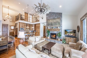 A spacious living area with a fireplace, a dining table, and a high ceiling fan.