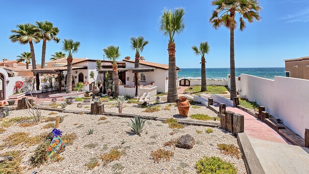 A coastal property with a patio area, palm trees, and a view of the sea.