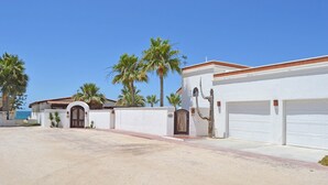 A residential area with a white building featuring a garage, palm trees, and a clear blue sky.
