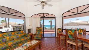 A room with a sofa, dining table, and chairs, a ceiling fan, and a view of the ocean.
